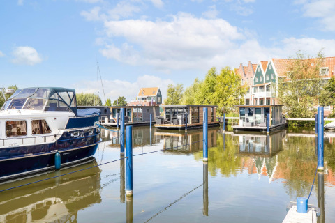 Woonboten en jachten in de Volendam Marina, Nederland, met kleurrijke huizen op de achtergrond.