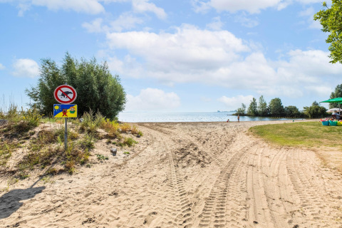 Chemin de sable menant à la plage près d'une péniche à Volendam Marina, vue sur l'eau et panneaux.