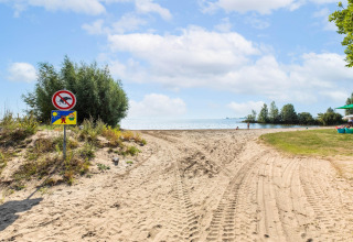 Sandweg zum Strand in Volendam Marina, Niederlande, mit Schildern und Blick auf das ruhige Wasser.