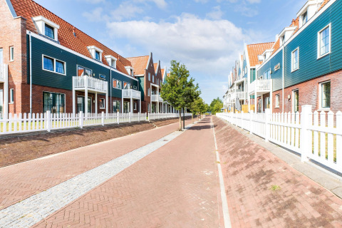 Moderne rækkehuse med røde tage og hvide hegn i Volendam Marina, Holland, under en blå himmel.
