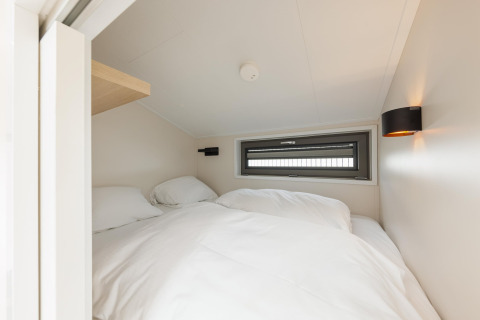 Lyst og hyggeligt soveværelse med skrå loft, vindue og hvidt sengetøj i Beach Houses Zandvoort 2.