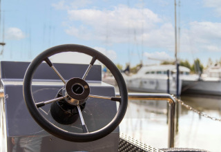 Roue de direction d'une péniche à Volendam Marina, Pays-Bas, avec vue sur l'eau et les bateaux.