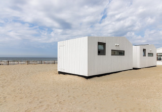 Et hvidt strandhus kaldet Beach Houses Zandvoort 2 på sandet strand i Holland med havet i baggrunden.