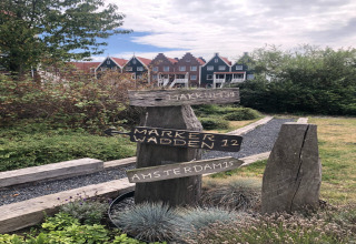 Panneau en bois à la marina de Volendam indiquant Makkum, Marker Wadden et Amsterdam, maisons derrière.