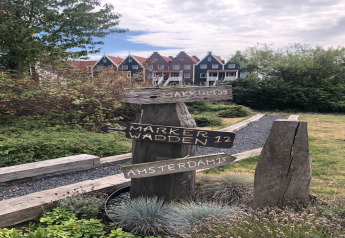 Panneau en bois à la marina de Volendam indiquant Makkum, Marker Wadden et Amsterdam, maisons derrière.