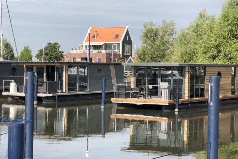Husbåde ligger fortøjet på stille vand foran et hus ved Volendam Marina i Nederlandene.