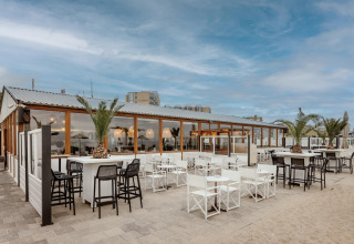 Udendørs strandhusrestaurant med palmer og moderne møbler, klar til gæster under en blå himmel.