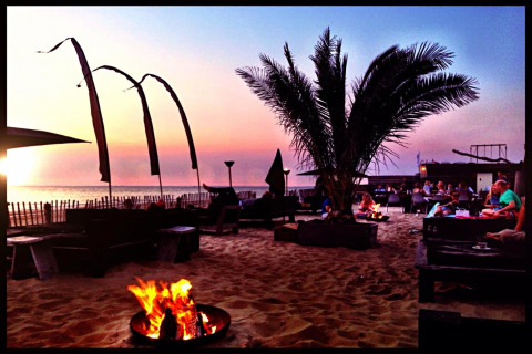 Solnedgang ved Beach Houses Zandvoort 2 i Nederlandene, med bål, palme og gæster, afslappet strandmiljø.