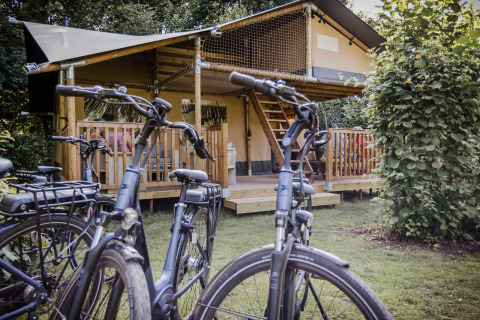 Tienda safari Ranger Lodge en Baalse Hei, Bélgica, con bicicletas estacionadas frente a un porche de madera.