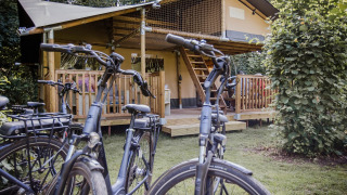 Tienda safari Ranger Lodge en Baalse Hei, Bélgica, con bicicletas estacionadas frente a un porche de madera.