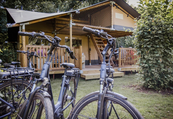 Tienda safari Ranger Lodge en Baalse Hei, Bélgica, con bicicletas estacionadas frente a un porche de madera.