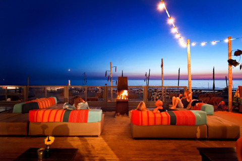 Aftenstemning ved Beach Houses Zandvoort 2 i Holland, med folk på sofaer ved bål og udsigt til stranden.