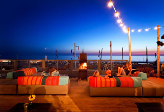 Aftenstemning ved Beach Houses Zandvoort 2 i Holland, med folk på sofaer ved bål og udsigt til stranden.