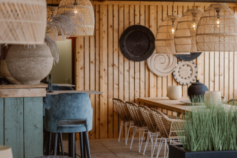 Moderne strandhustema med trævægge, fletlamper, stilfulde stole og naturnær dekoration i lyse nuancer.
