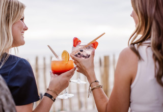 To kvinder skåler med farverige cocktails foran stranden ved Beach Houses Zandvoort 2 i Holland.