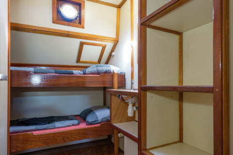Slaapkamer met stapelbedden, planken en patrijspoort op een woonboot in Leiden, Nederland.