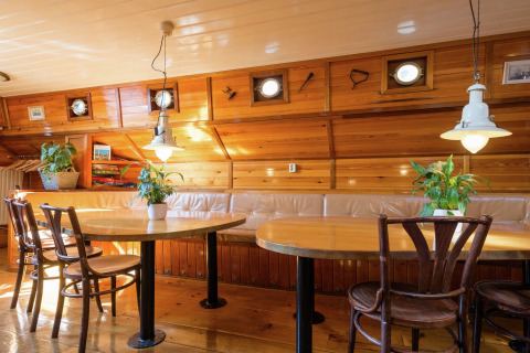 Licht en gezellig interieur van een woonboot in Leiden met houten wanden, ronde ramen en planten.