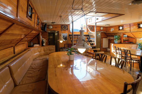 Sfeervol interieur van woonboot met houten afwerking, eethoek en veel daglicht in Leiden.