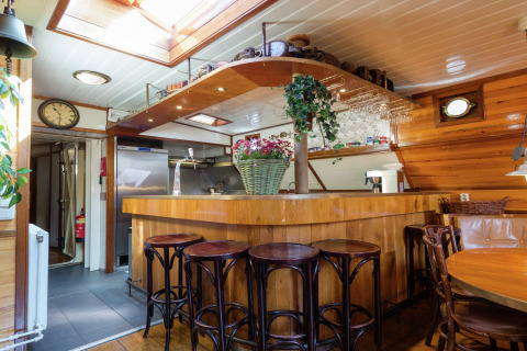 Gezellige barhoek in een woonboot te Leiden, Nederland, met houten afwerking en barkrukken.