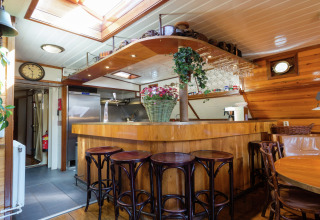 Sfeervolle bar in een woonboot in Leiden, Nederland, met houten inrichting, barkrukken en planten.