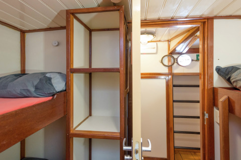 Slaapkamer op een woonboot in Leiden met stapelbedden, open rekjes en houten wandpanelen.