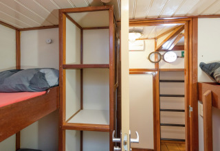 Schlafzimmer auf einem Hausboot in Leiden mit Etagenbetten, offenen Regalen und Holzverkleidung.