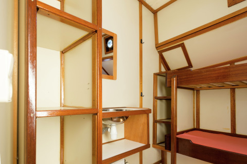 Interieur van een woonboot in Leiden met stapelbed, open houten planken en een kleine wastafel.