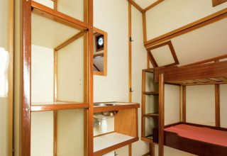 Interieur van een woonboot in Leiden met stapelbed, open houten rekken en een kleine wasbak.