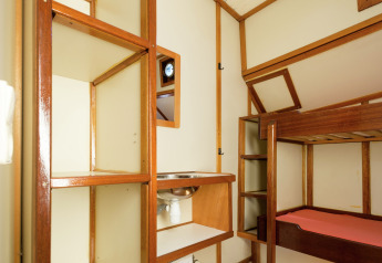 Innenraum eines Hausbootes in Leiden mit Etagenbett, offenen Regalen, kleinem Waschbecken und Holzdetails.