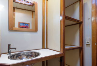 Badkamer op een woonboot in Leiden met moderne wasbak, spiegel, open rekken en stopcontact.
