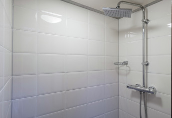 Ducha moderna con azulejos blancos y cabezal metálico en una casa flotante en Leiden cerca del centro y museos.