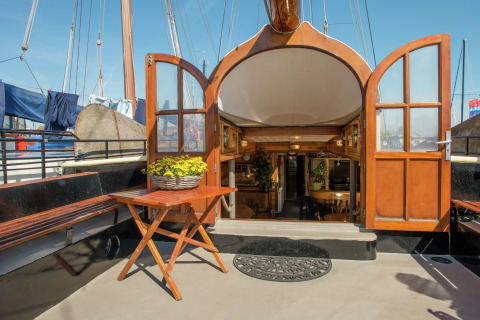 Eingang zur Hausboot in Leiden mit offenen Holztüren, Tisch, Bank und gemütlichem Interieur sichtbar.