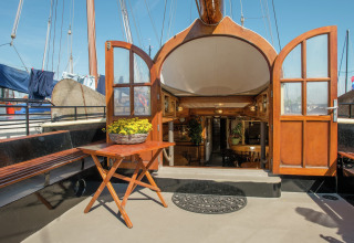Entree van woonboot in Leiden met open houten deuren, tafel, bank en sfeervol interieur met planten.