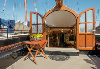 Entrada a casa flotante en Leiden con puertas de madera abiertas, mesa, banco y interior acogedor con plantas.