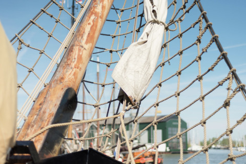 Nahaufnahme von Taunetz und Holzmast auf einem Hausboot in Leiden mit Hafen und Gebäuden im Hintergrund.