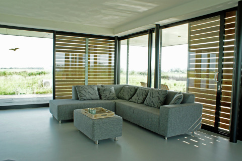 Moderne stue på husbåd med grå sofa, store vinduer, udsigt over naturen, Watervilla de Blauwe Reiger, Holland.