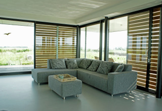 Moderne stue på husbåd med grå sofa, store vinduer, udsigt over naturen, Watervilla de Blauwe Reiger, Holland.