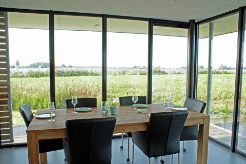 Spisebord med sorte stole og glasfacade, med udsigt til frodige marker i Watervilla de Blauwe Reiger.