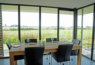 Spisebord med sorte stole og glasfacade, med udsigt til frodige marker i Watervilla de Blauwe Reiger.