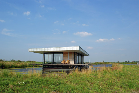 Moderne husbåd, Watervilla de Blauwe Reiger, på stille vandvej i Holland med blå himmel og græs.