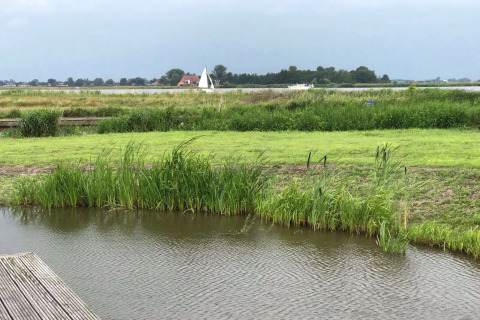 Udsigt over en flod og grønne enge fra husbåden Watervilla de Blauwe Reiger i Holland.