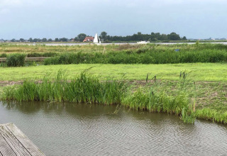 Udsigt over en flod og grønne enge fra husbåden Watervilla de Blauwe Reiger i Holland.