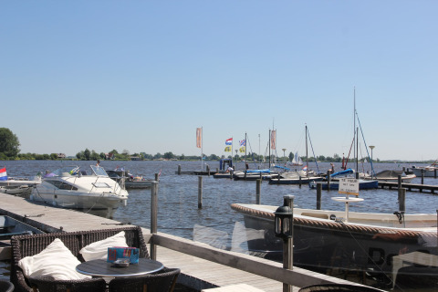 Udsigt fra Watervilla de Blauwe Reiger i Holland med både, havn og udendørs siddeplads i solskin.