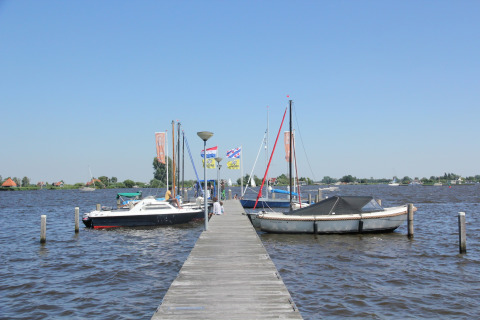 Træmole med lystbåde og flag ved Watervilla de Blauwe Reiger, under en klar blå himmel i Holland.