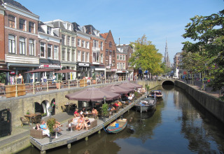 Hus både ved kanalen med folk der nyder caféer og solskin, Watervilla de Blauwe Reiger, Holland.