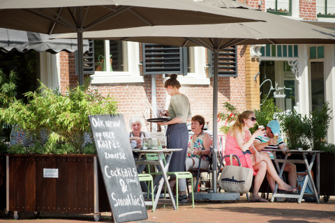 Udendørs café ved Watervilla de Blauwe Reiger i Holland, folk nyder drinks under store parasoller.
