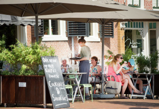 Udendørs café ved Watervilla de Blauwe Reiger i Holland, folk nyder drinks under store parasoller.
