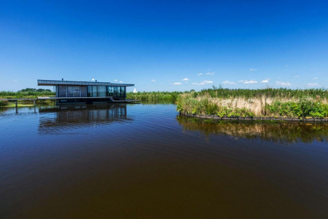 Hus på vandet kaldet Watervilla de Blauwe Reiger i Holland, omgivet af natur og klart blåt himmel.