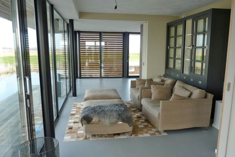 Moderne stue på husbåd Watervilla de Blauwe Reiger i Holland med store vinduer og beige møbler.