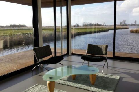 Moderne stue på husbåd Watervilla de Blauwe Reiger med store vinduer og udsigt til vand og natur i Holland.